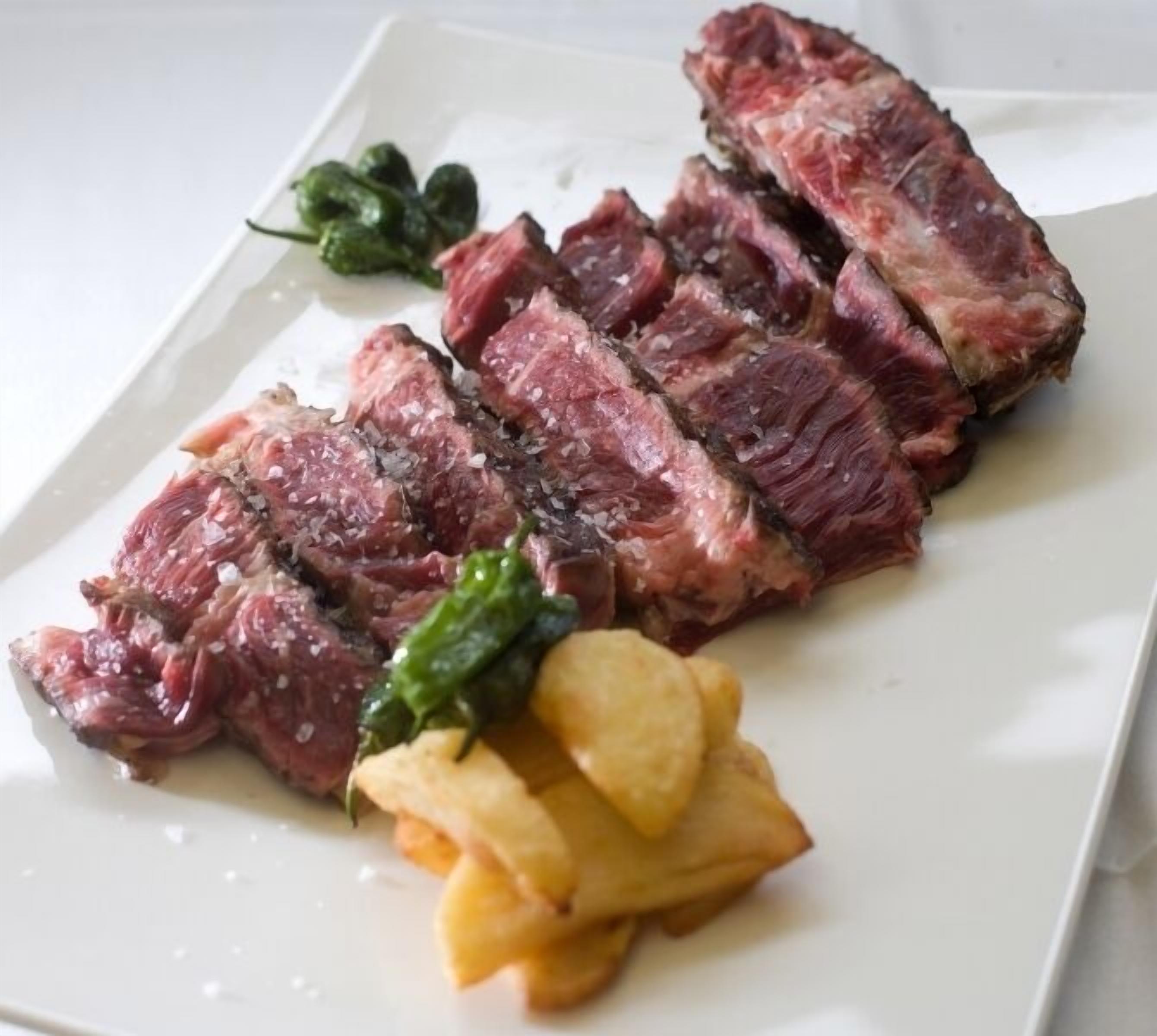 Un plato con bistec en rodajas, verduras verdes y patatas fritas.