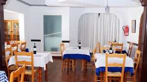 A dining area with wooden chairs and tables, each covered with a white tablecloth and blue table runner. - Hospedería Ancladero (Mojacar)