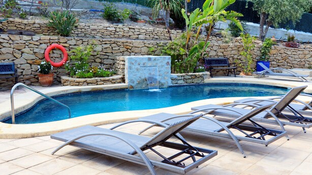 A swimming pool with a stone wall, lounge chairs, and a small waterfall feature. - Hospedería Ancladero (Mojacar)