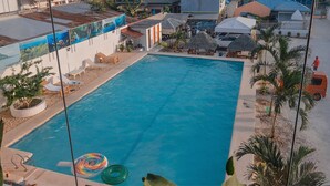 A swimming pool with lounge chairs and umbrellas, surrounded by buildings and palm trees. - Adams View Hotel (Moalboal)