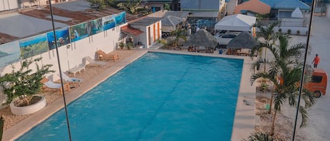 A swimming pool with lounge chairs and umbrellas, surrounded by buildings and palm trees.