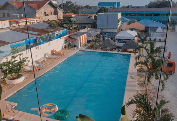 A swimming pool with lounge chairs and umbrellas, surrounded by buildings and palm trees. - Adams View Hotel (Moalboal)