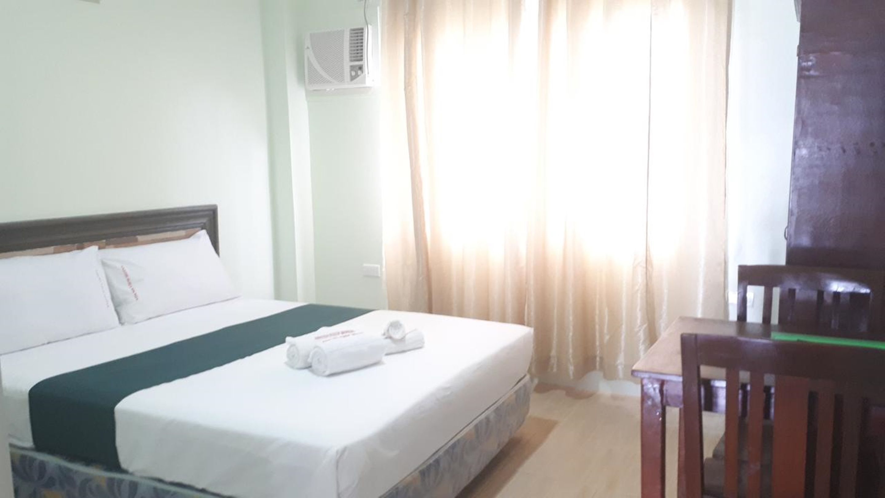Una habitación de hotel con una cama, una silla de madera y una ventana con cortinas.