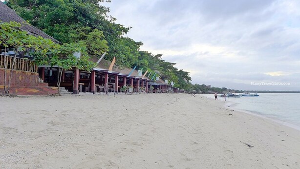 A beach with a row of wooden buildings, some with thatched roofs, along the shoreline. - Adams View Hotel (Moalboal)