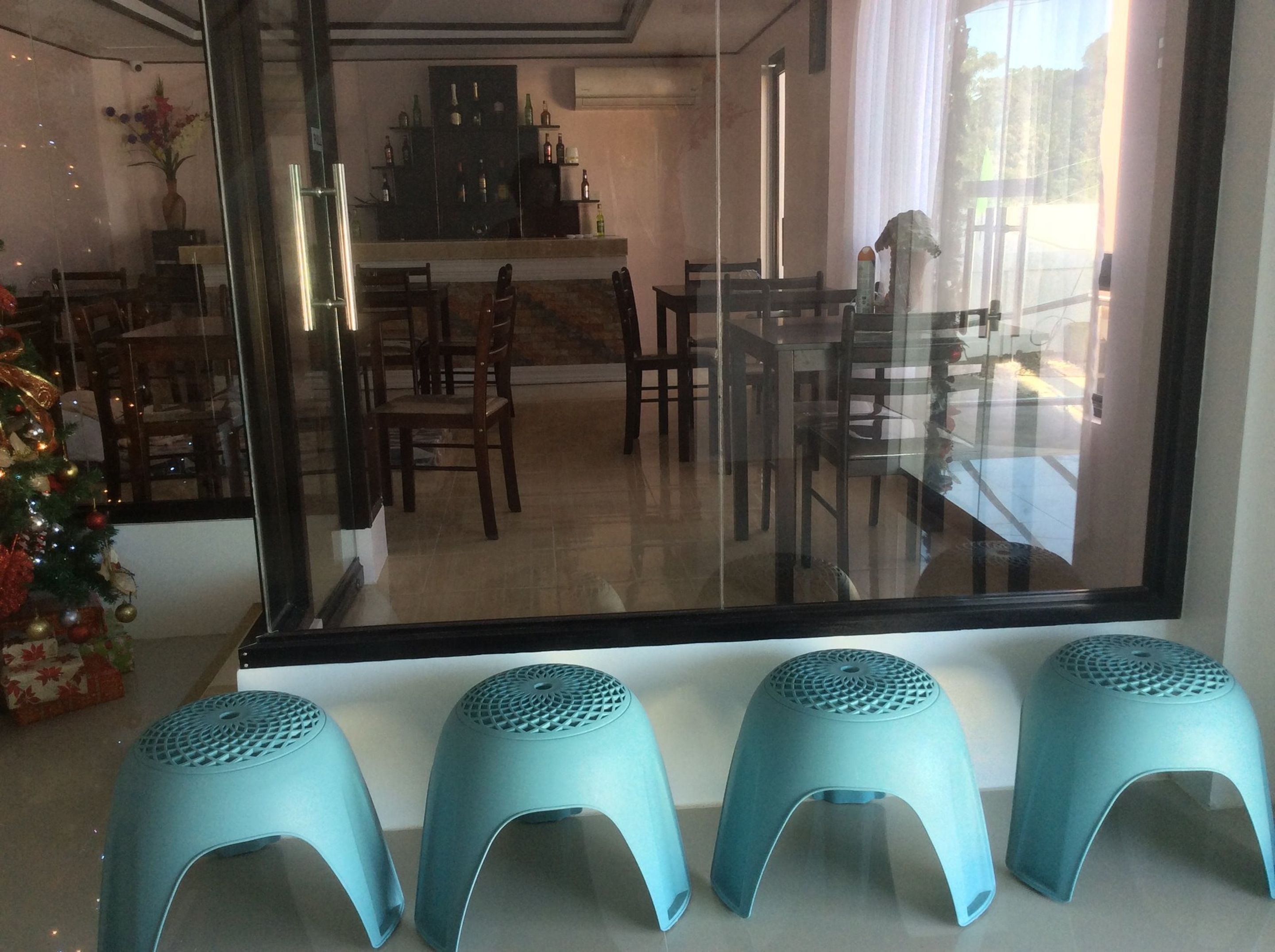 Un espace repas séparé par une cloison en verre, un sapin de Noël et trois tabourets bleus.