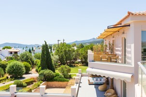 A modern villa with a balcony overlooking a landscaped garden and a mountainous backdrop.