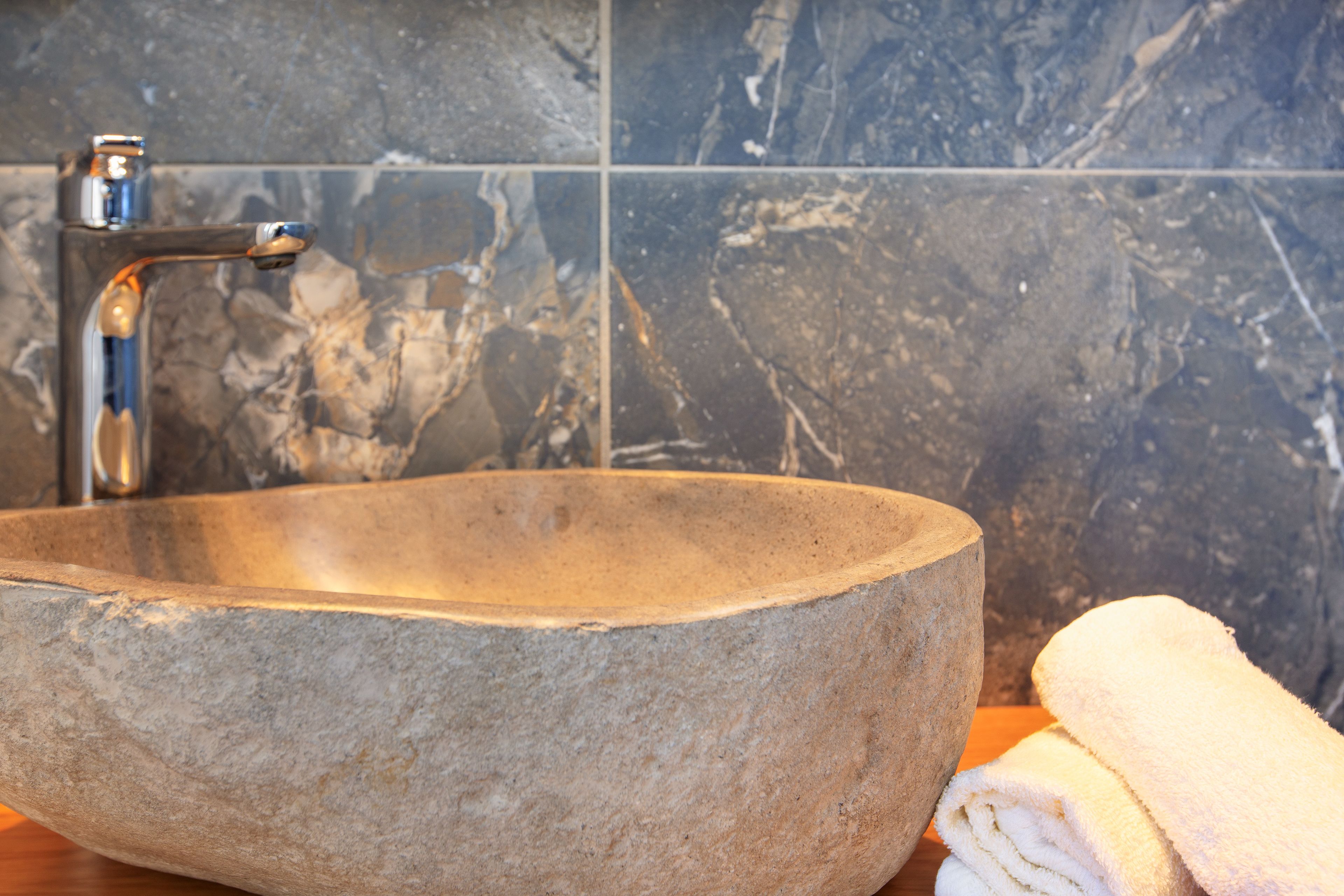 A stone sink with a modern faucet in a bathroom with dark marble tiles.
