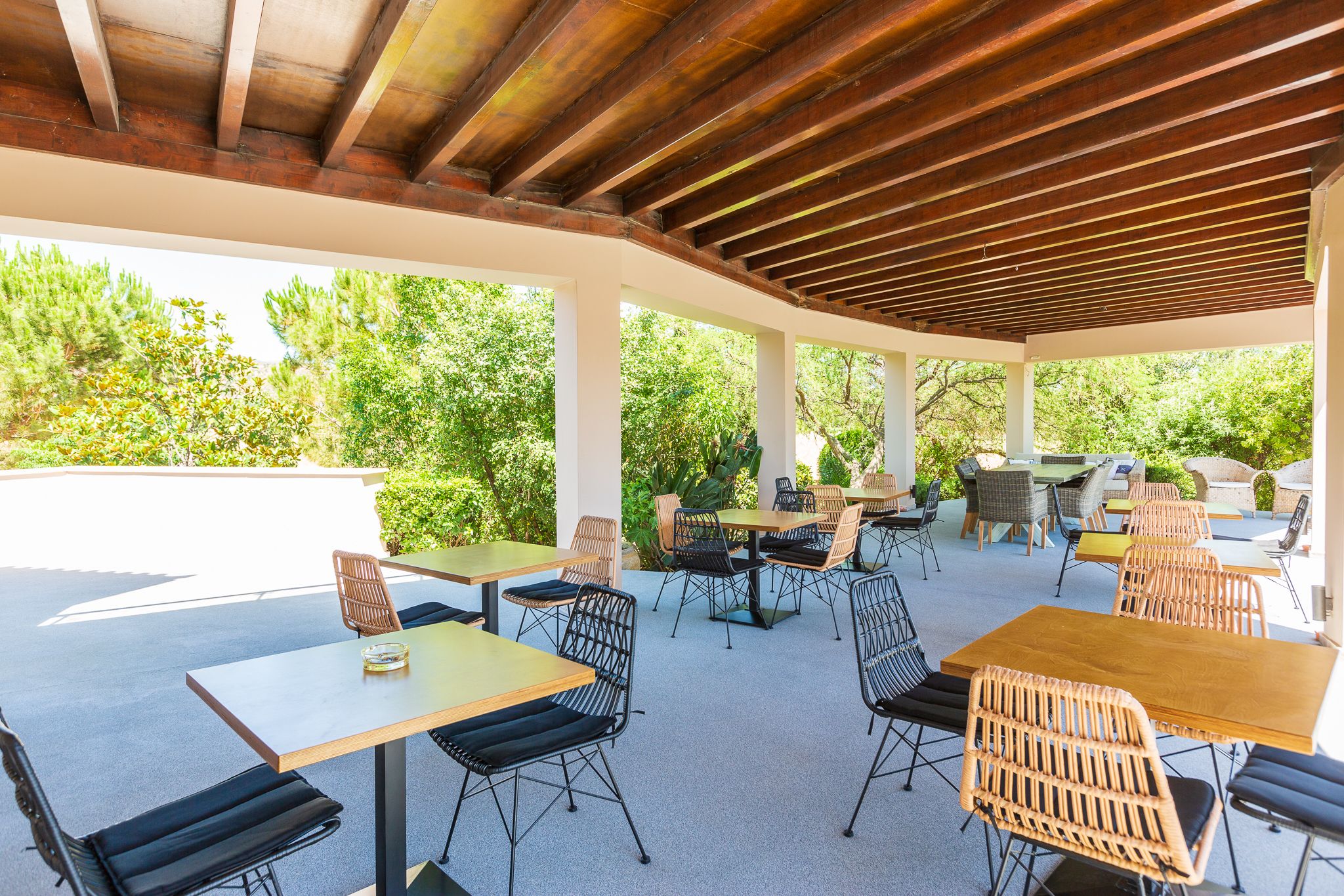 An outdoor patio with tables and chairs, surrounded by greenery.