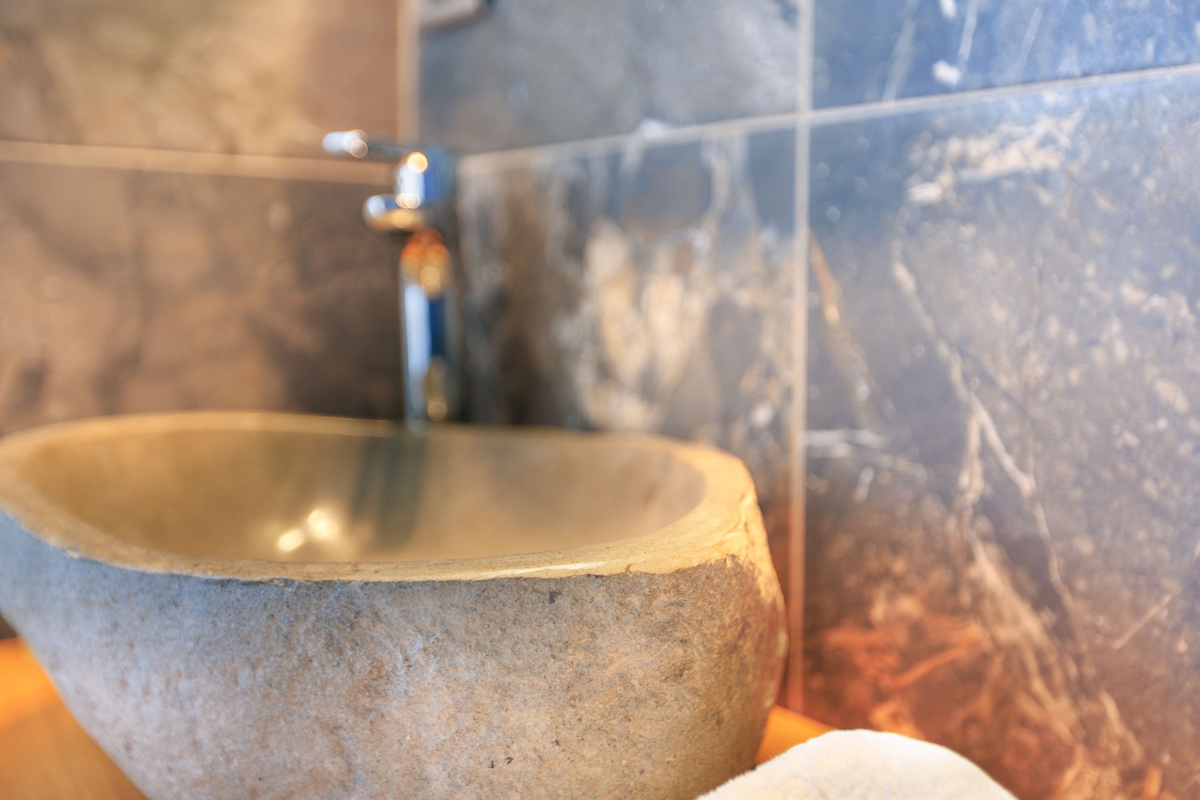 A stone basin with a faucet in a bathroom with marble walls.