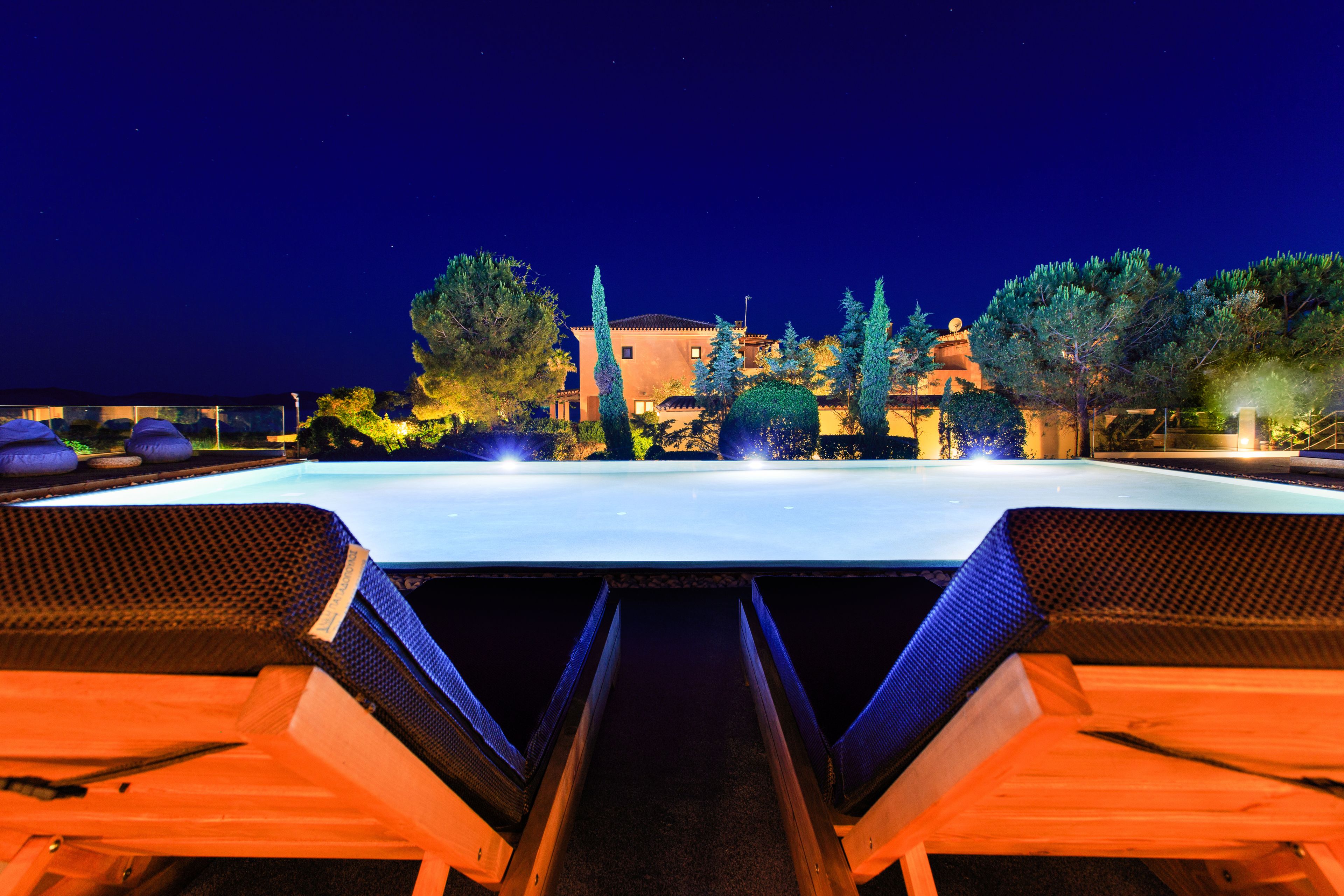 A nighttime view of a swimming pool with lounge chairs and a building in the background.