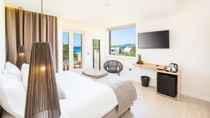 Ein modernes Hotelzimmer mit einem großen Bett, einem Fernseher, einem kleinen Schreibtisch und Meerblick.