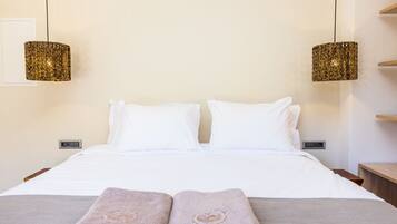 A hotel room with a bed, two white pillows, two towels with text, two hanging lamps, and a bedside table.