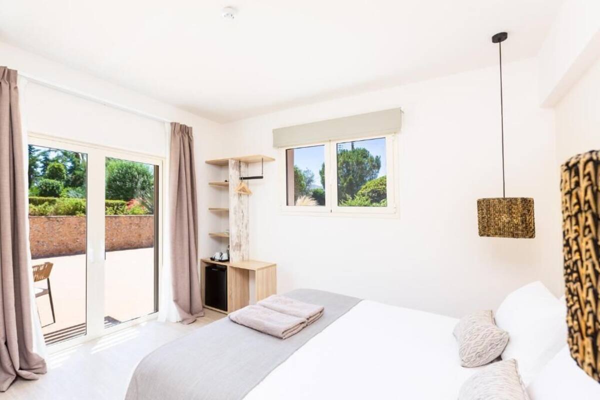 Une chambre avec un lit, un bureau, une chaise et une vue sur la verdure par la fenêtre.