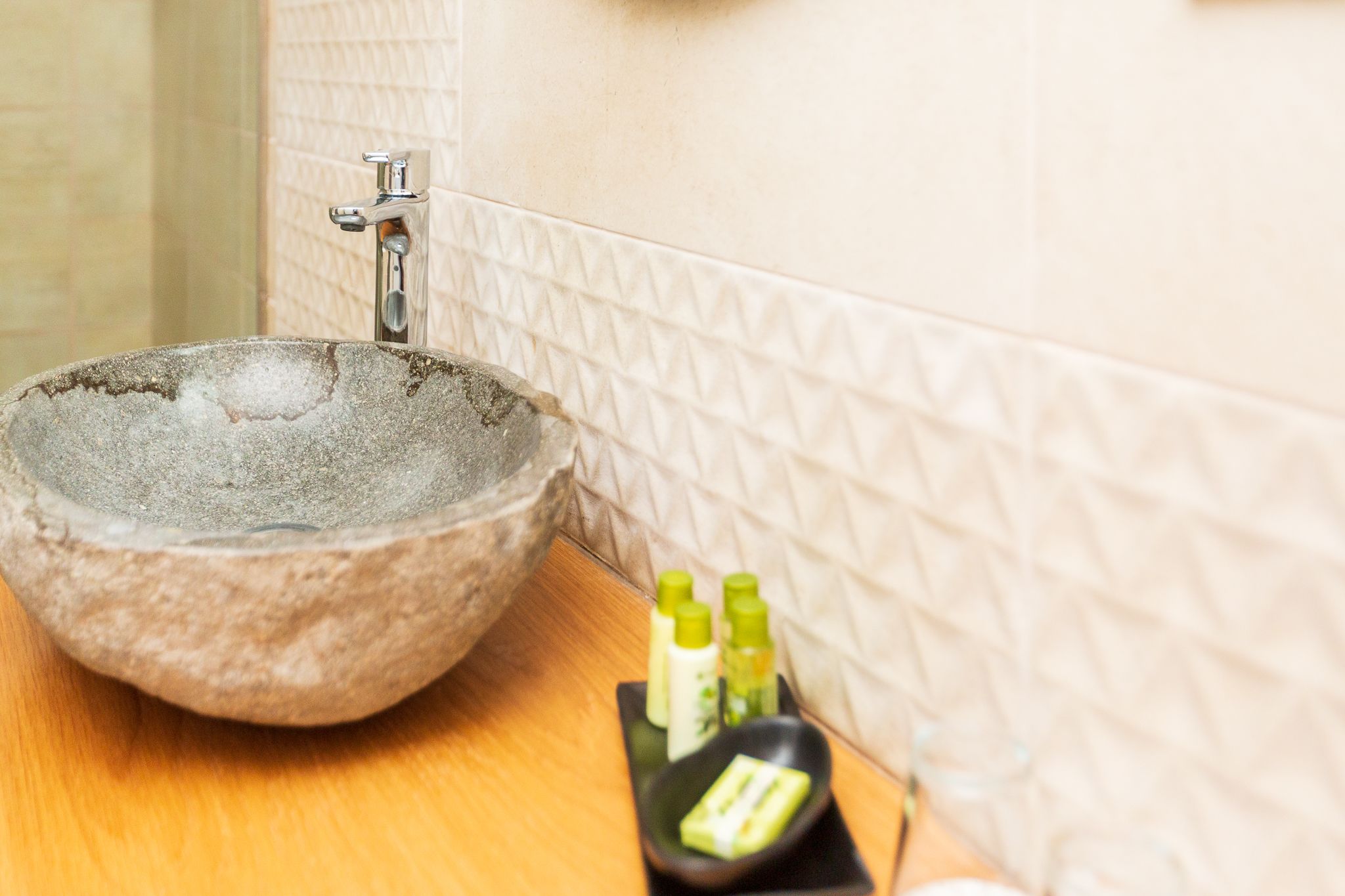 Un lavabo de piedra con un grifo, una bandeja con artículos de tocador y una pared con azulejos.