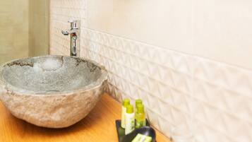 Un lavabo de piedra con un grifo, una bandeja con artículos de tocador y una pared con azulejos.