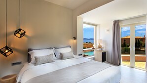 Ein modernes Schlafzimmer mit einem großen Bett, einem Nachttisch, einer Lampe und Blick ins Freie.