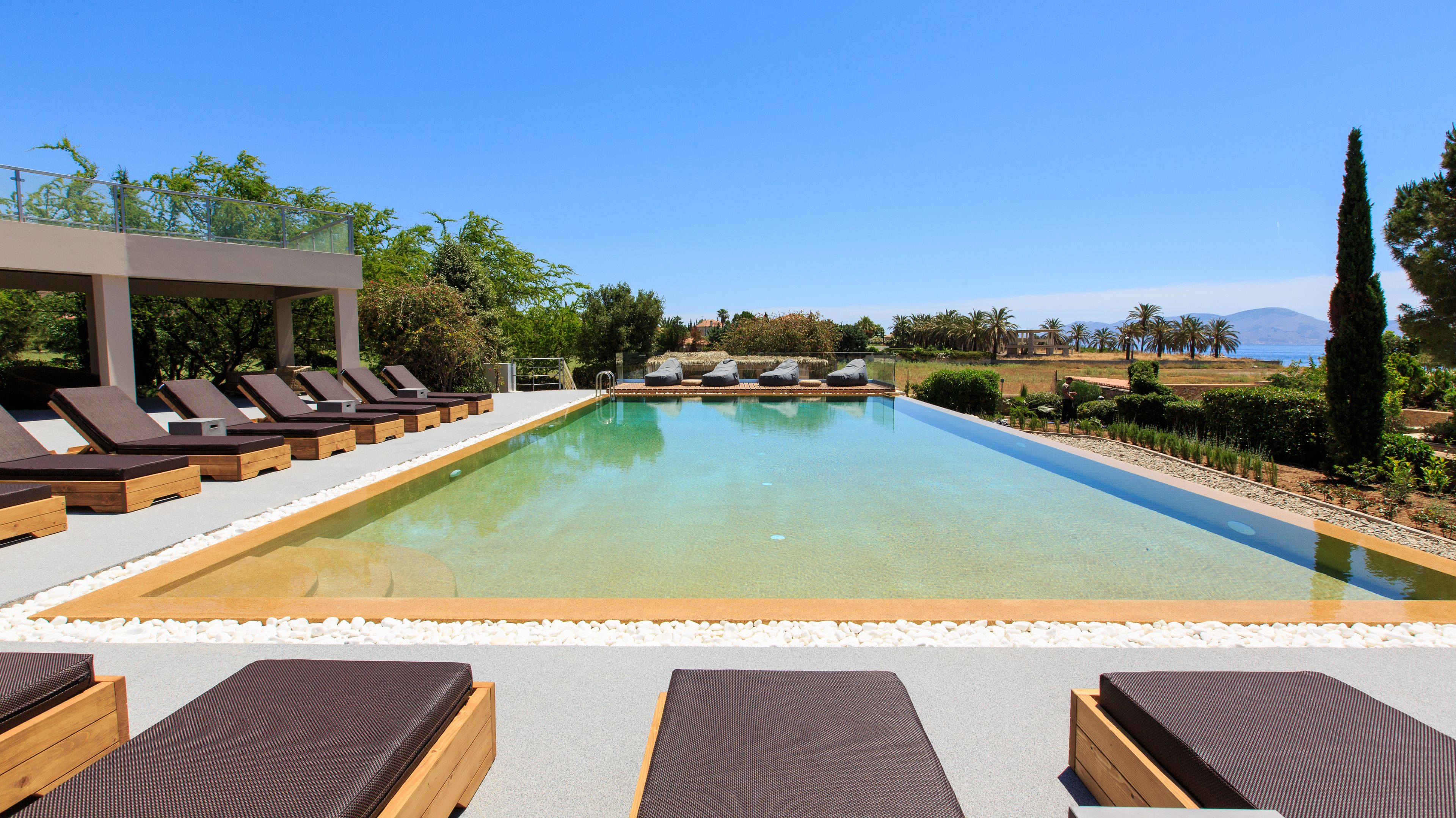 A swimming pool with lounge chairs and a pergola, surrounded by greenery and a clear view of the landscape.