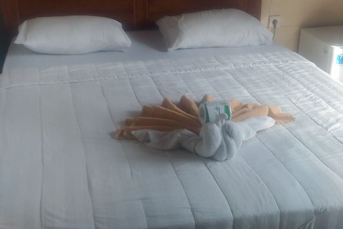 A neatly made bed with white linens and a wooden headboard.