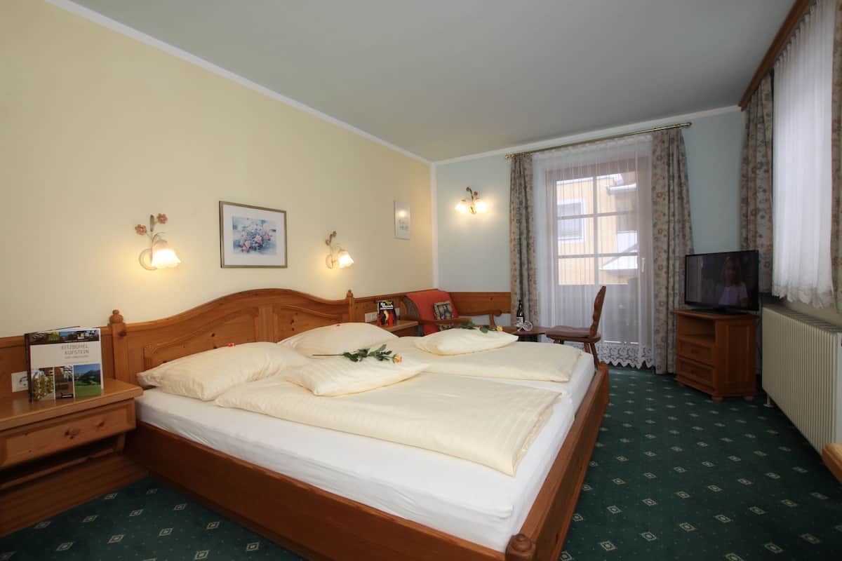 A double bed with a wooden headboard, two bedside tables, a nightstand, a television, and a window with curtains.