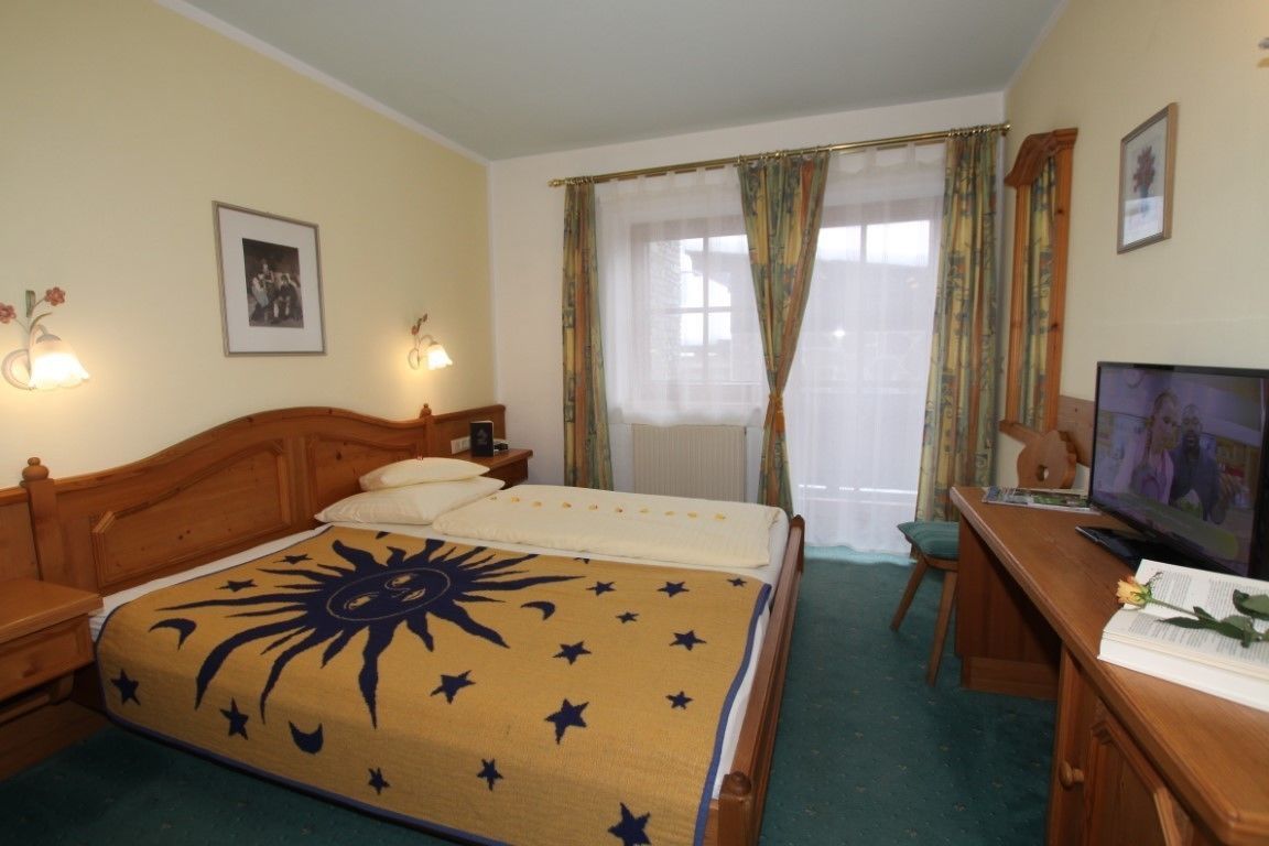A hotel room with a bed, a desk with a television, a chair, and a window with curtains.