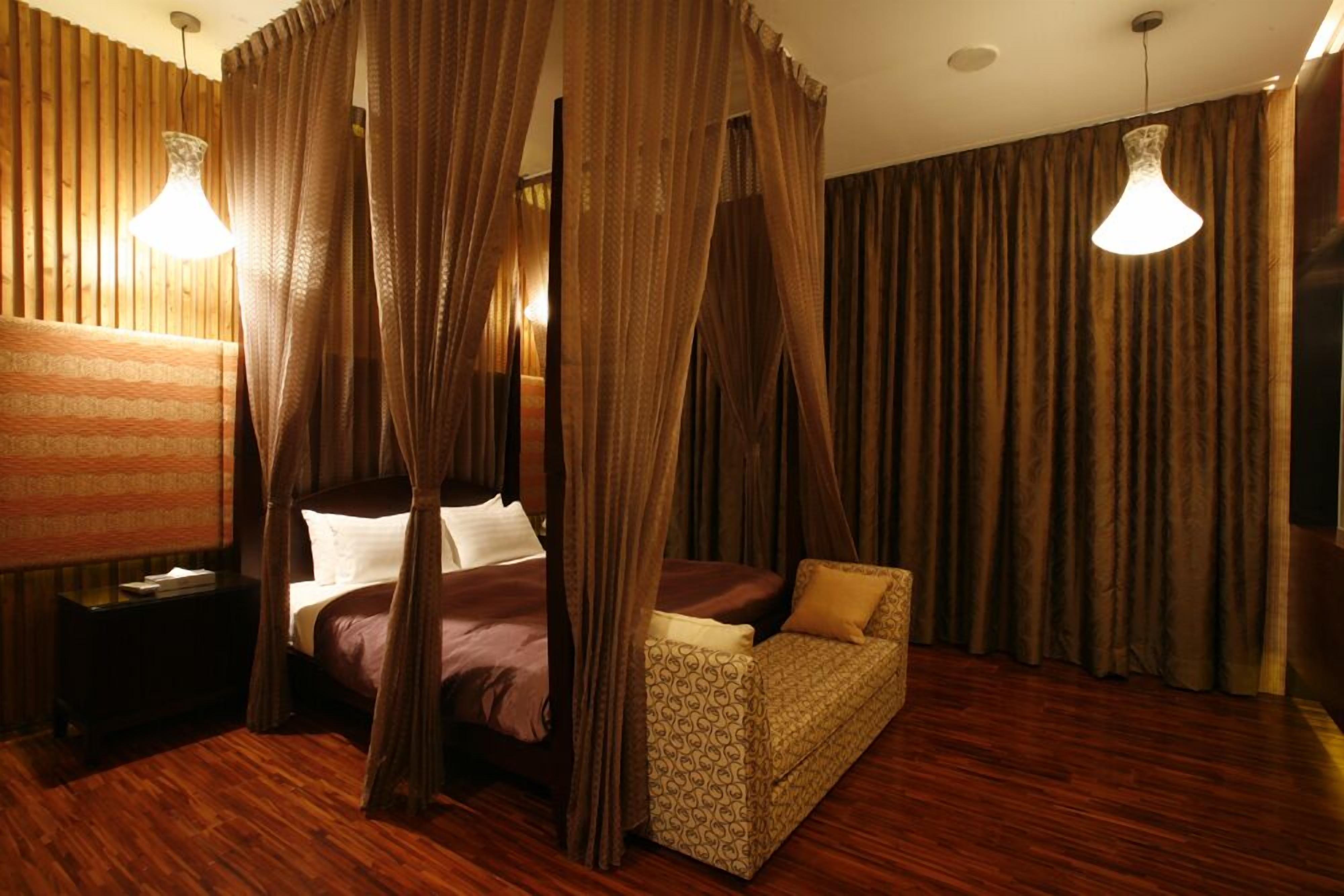 A four-poster canopy bed with a headboard, a bedside table, and a patterned sofa.