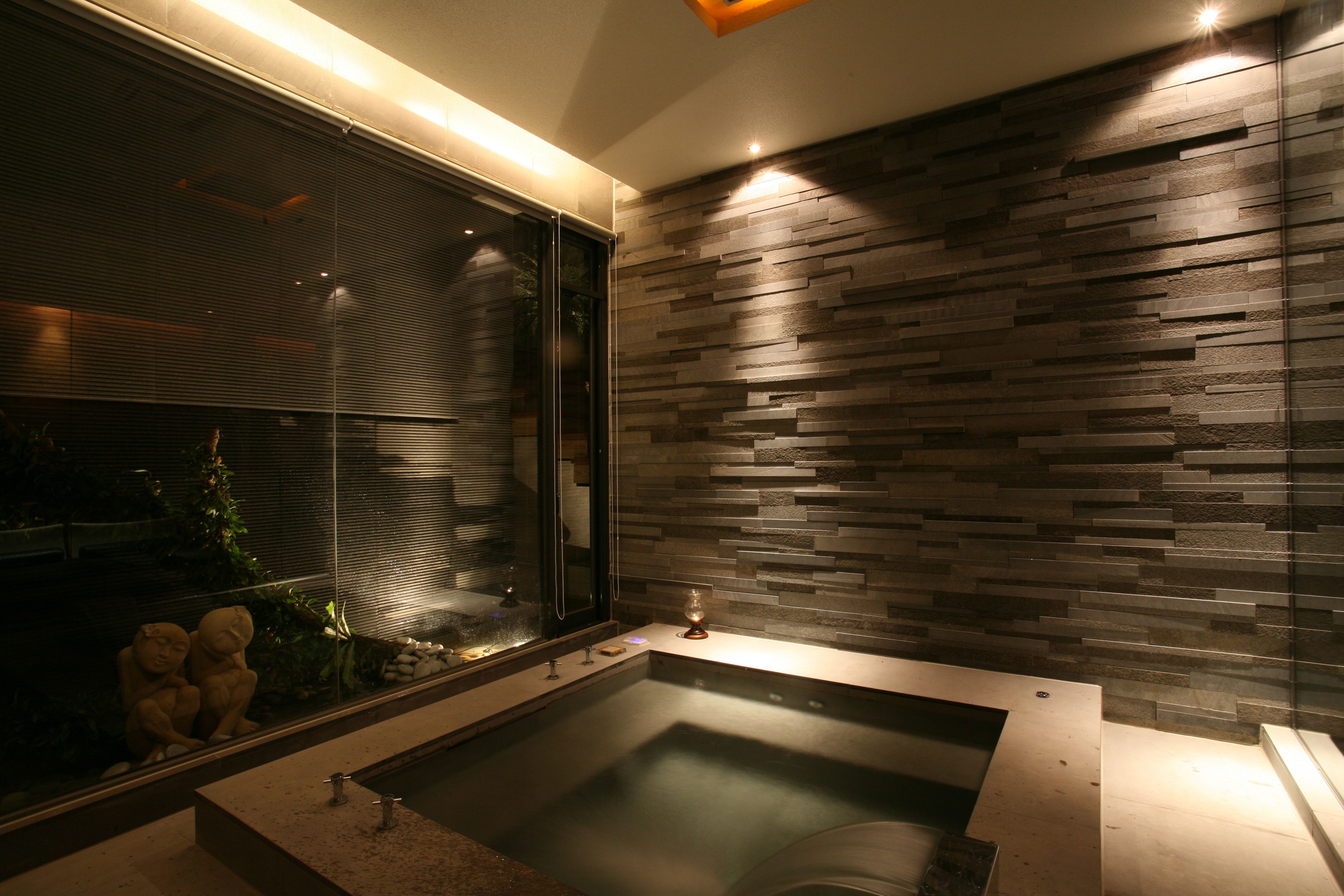 A modern bathroom with a large bathtub, a window with blinds, and a wall with a wood-like texture.