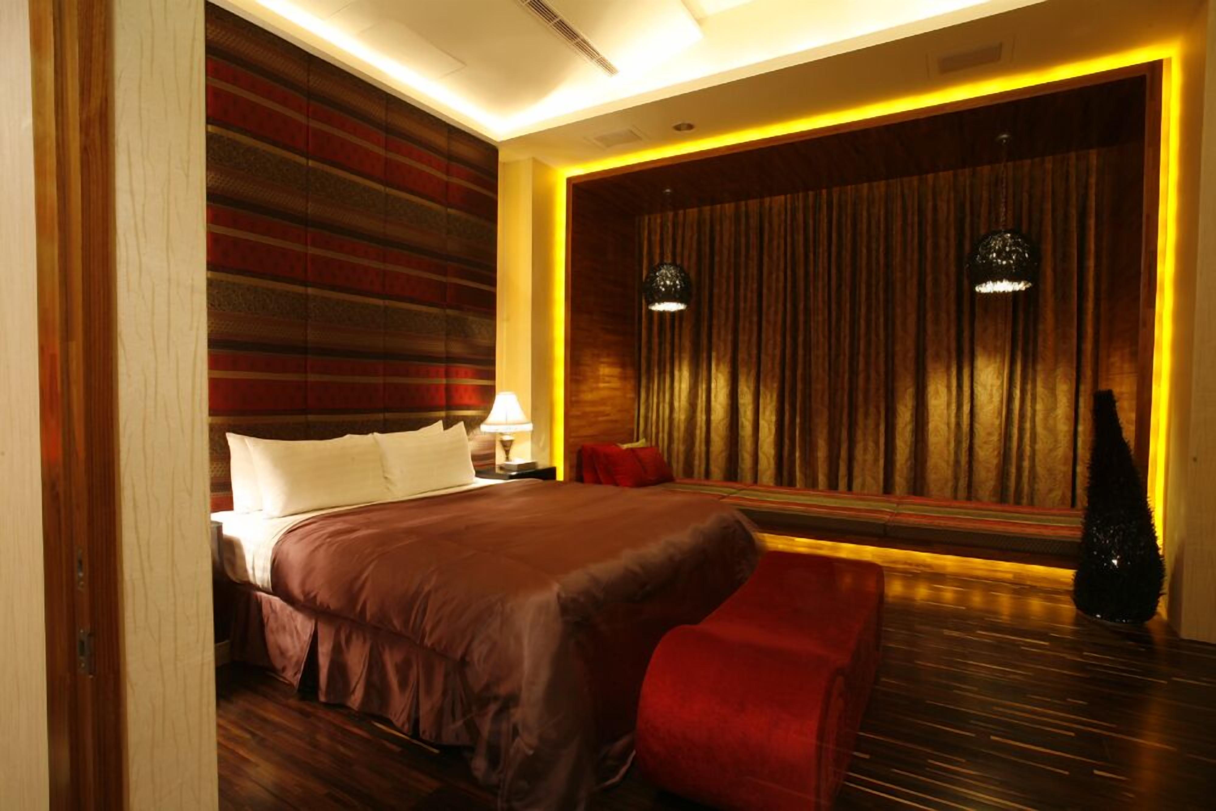 Ein modernes Hotelzimmer mit einem großen Bett, einem roten Sessel, einem Nachttisch mit Lampe und einer Wand mit Vorhängen.