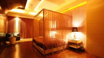 A modern bedroom with a four-poster bed, a bedside table with a lamp, and a potted plant.