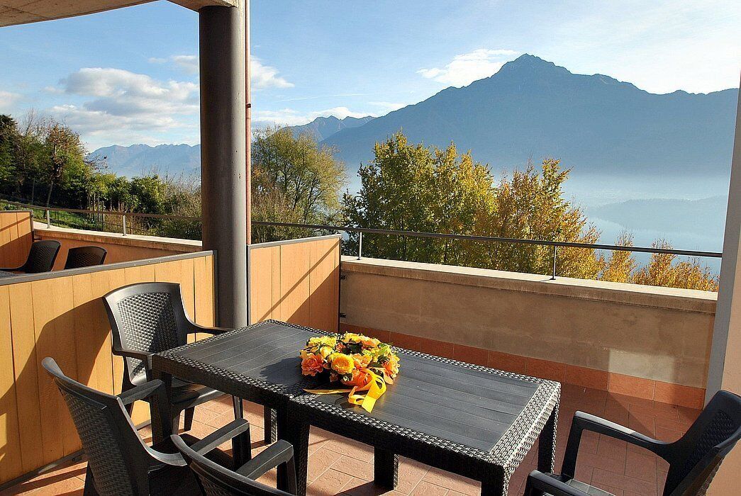 Um terraço com mesa e cadeiras, um buquê de flores e vista para montanhas e um lago.