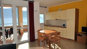 A compact kitchen with a dining area, a sliding glass door leading to a balcony, and a TV in a wooden cabinet. - Casa Osmanto I: A cozy and welcoming apartment situated at a short distance from the shores of Lake Como, with Free WI-FI. (Domaso)