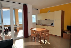 Una cocina compacta con comedor, una puerta corrediza de vidrio que da a un balcón y un televisor en un mueble de madera.
