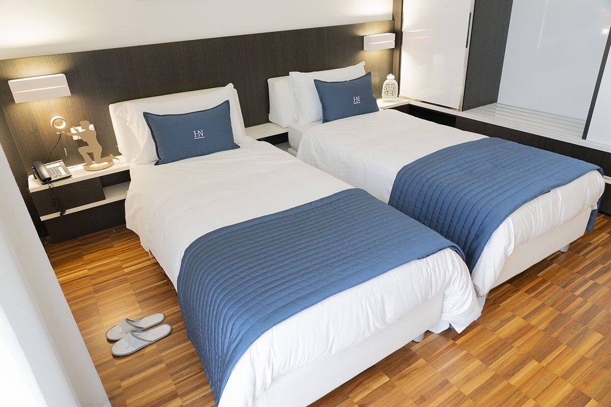 A hotel room with two beds, a wooden floor, a nightstand with a phone, and a wardrobe.