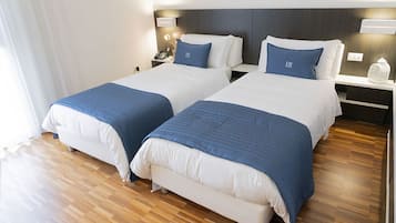 Ein Hotelzimmer mit zwei Betten, jedes mit einem blau abgesetzten Kissen, weißer Bettwäsche und Holzboden.