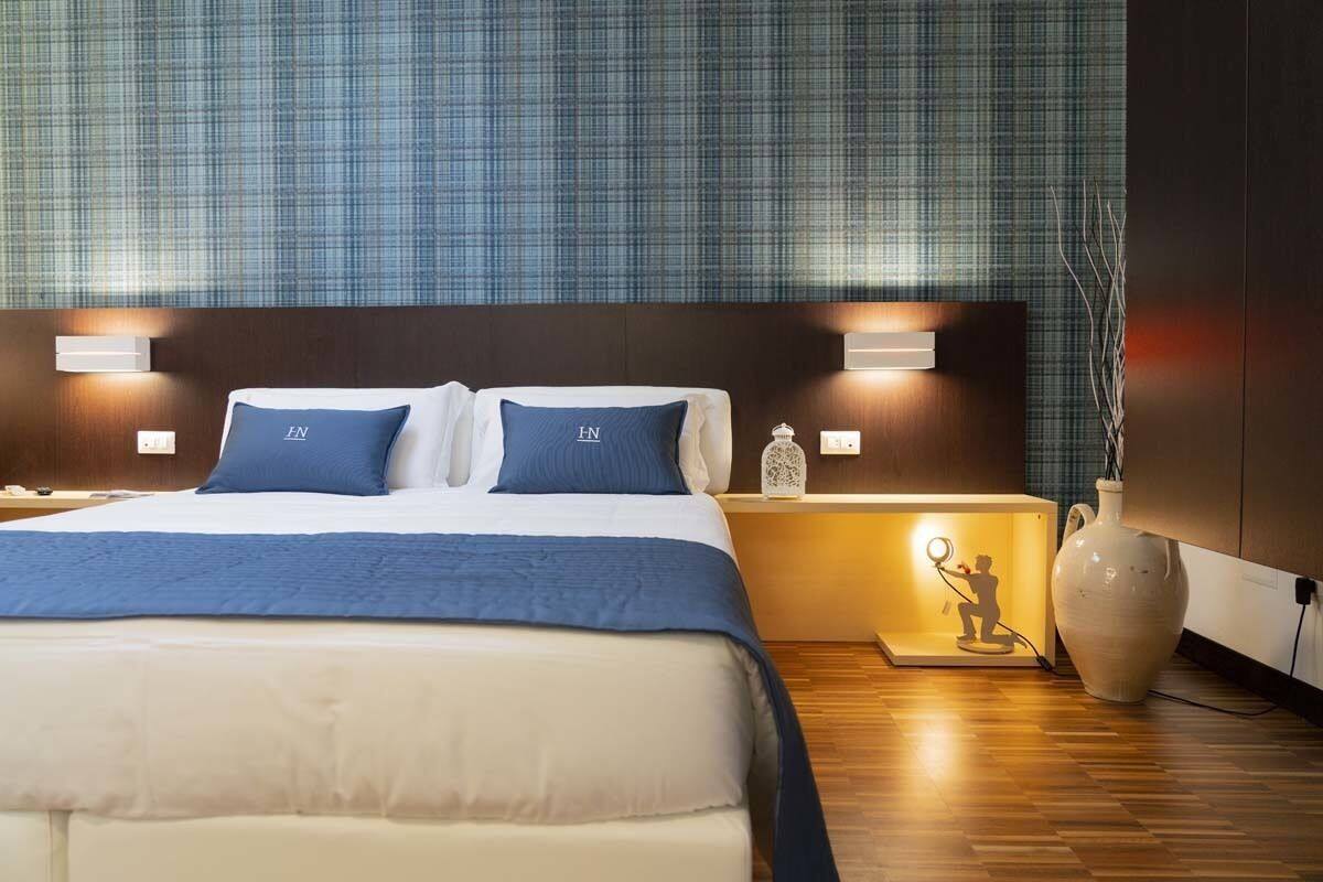 A hotel room with a large bed, two bedside tables with lamps, a nightstand with a decorative item, and a large vase.