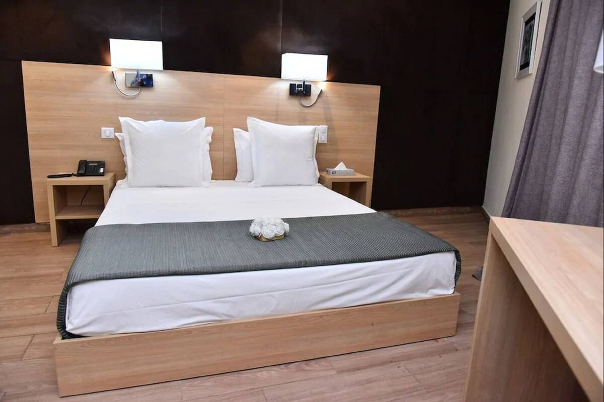 Uma cama de casal com cabeceira de madeira, duas mesas de cabeceira e uma pequena luminária.