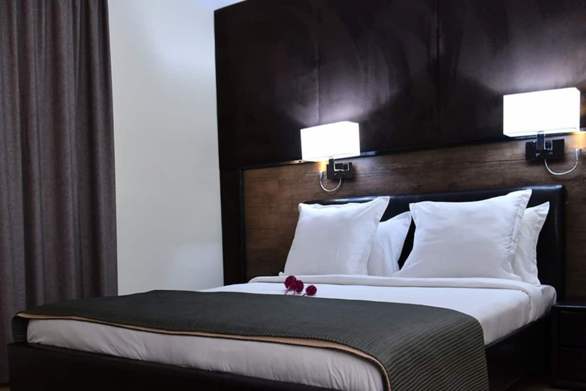 Quarto de hotel com uma cama grande, cabeceira de madeira escura, duas luminárias laterais e piso de madeira.
