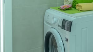 A front-loading washing machine with a control panel, a green mat, and a pink flower on top.