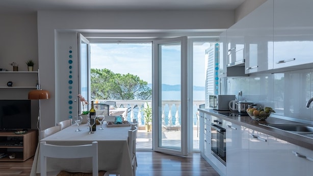 A modern kitchen with a dining area, large windows, and a view of the sea.