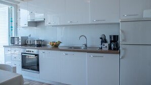 A modern kitchen with white cabinetry, a built-in oven, a microwave, a coffee maker, and a fruit bowl on the countertop.