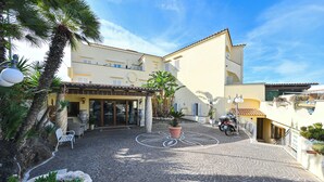 A cobblestone courtyard with a palm tree, a white chair, and a potted plant. - Hotel Terme Tramonto d'oro (Forio)
