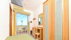 A room with a bed, a desk, a chair, a wardrobe, and a sliding glass door leading to an outdoor area with a table and chairs. - Hotel Terme Tramonto d'oro (Forio)