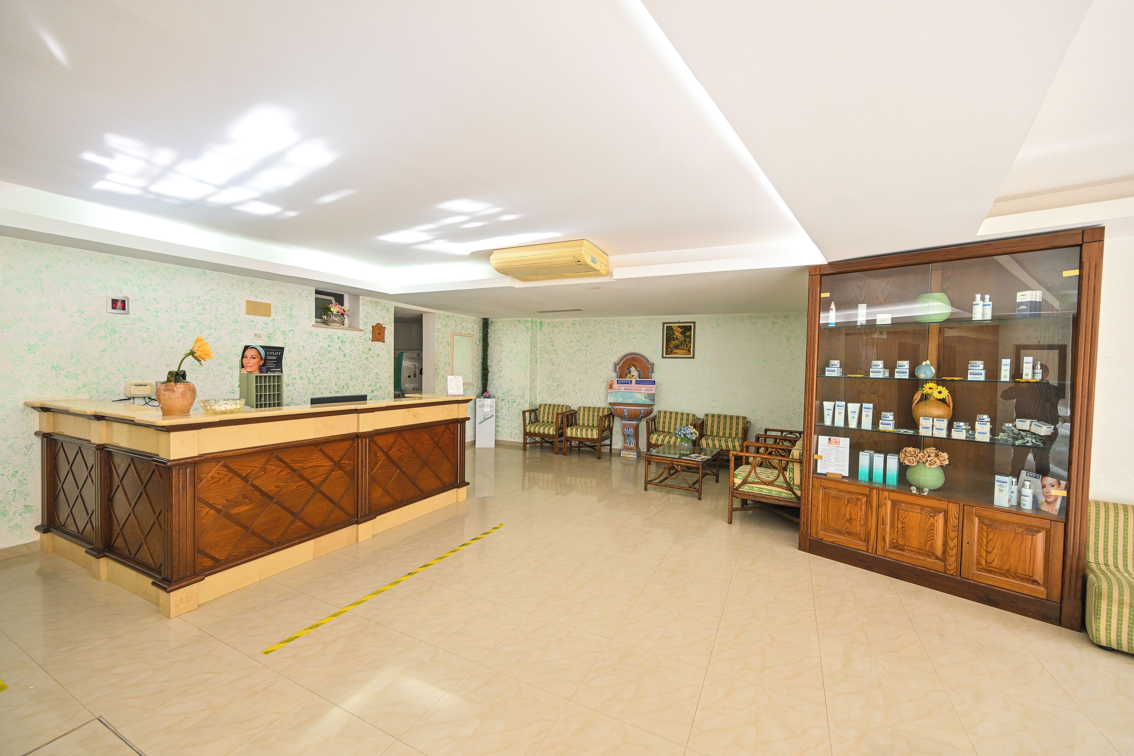 Un área de recepción con un mostrador de madera, varias sillas, un aparador con productos y un suelo de baldosas.