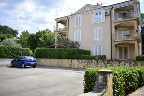 A multi-story building with balconies, a stone wall, and a parked car. - Apartment Diana (Malinska-Dubasnica)