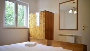 Une chambre à coucher avec un lit, une armoire en bois, un radiateur et une fenêtre donnant sur des arbres.