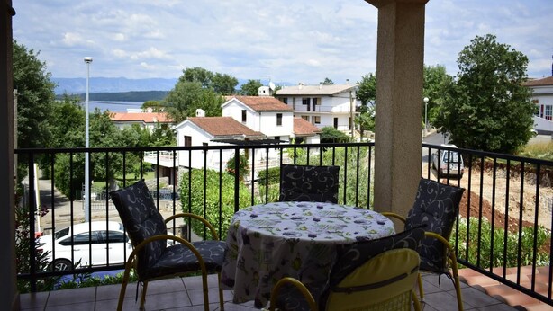 Un balcon avec une table et des chaises, donnant sur un quartier résidentiel avec des maisons et une route.