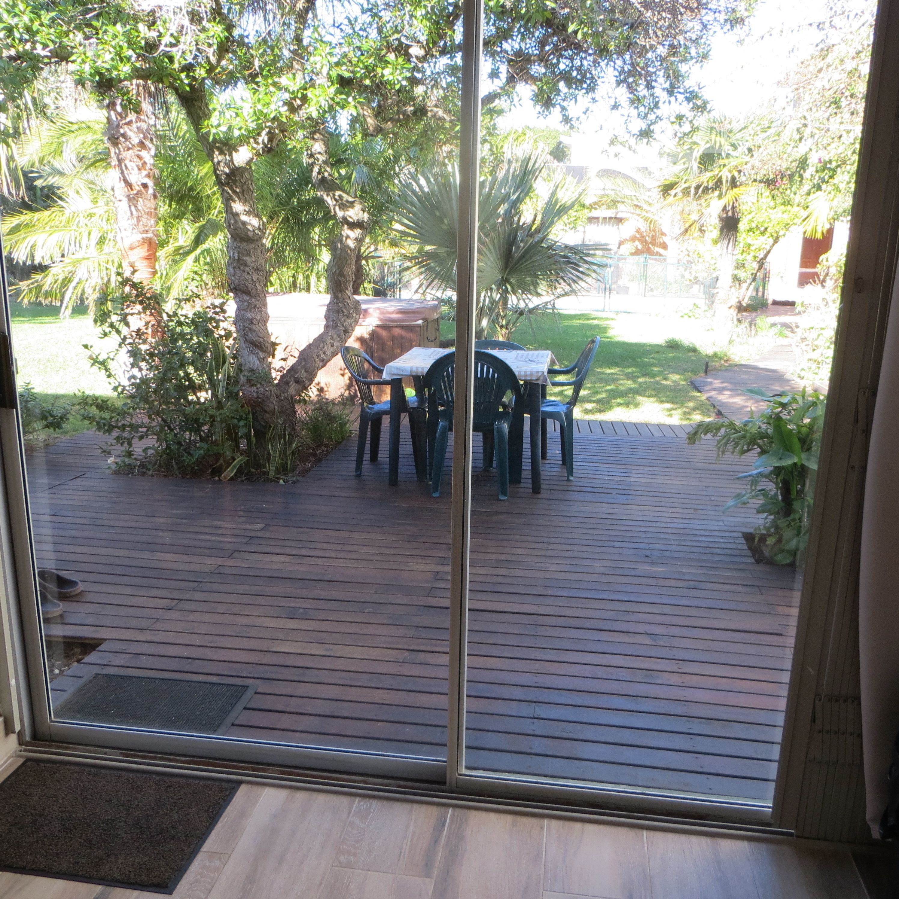 A wooden deck with a table and chairs, surrounded by trees and a grassy area.