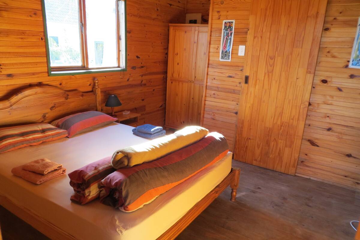 A wooden cabin bedroom with a bed, pillows, and a nightstand.