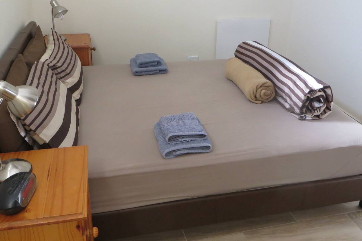 A neatly made bed with two folded towels, a striped pillow, and a rolled-up blanket.