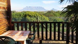 Um deck de madeira com mesa e cadeiras, com vista para um jardim exuberante e uma cordilheira.