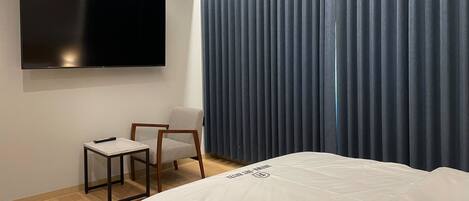 Habitación de hotel moderna con una cama grande, un televisor de pantalla plana en la pared, una mesita y una silla.